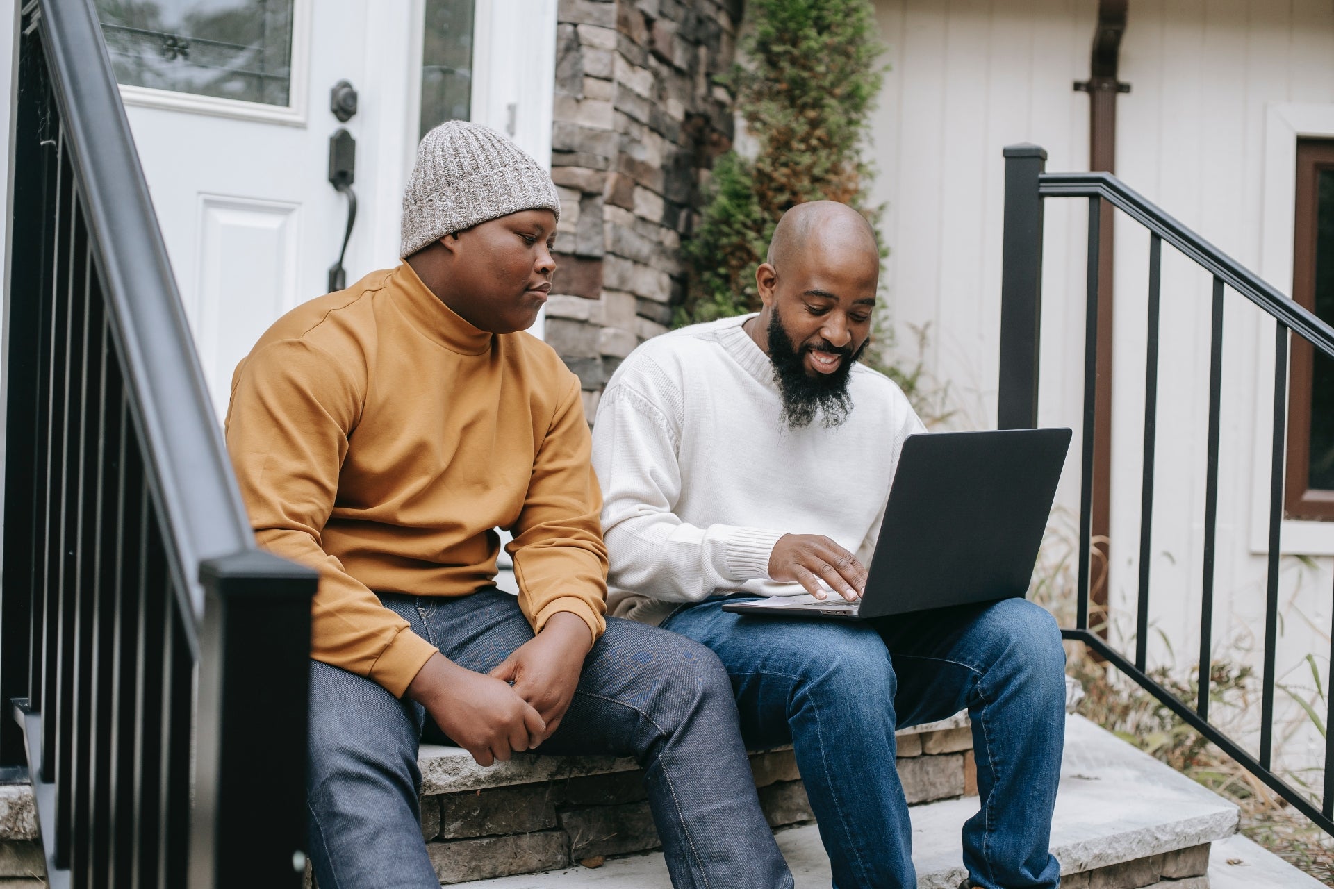 A father and teenage son sit out on a porch with a laptop discussing how to add rent and utilities to your credit report.
