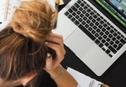 A birds eye view of a woman with her head in her hands and her open laptop screen