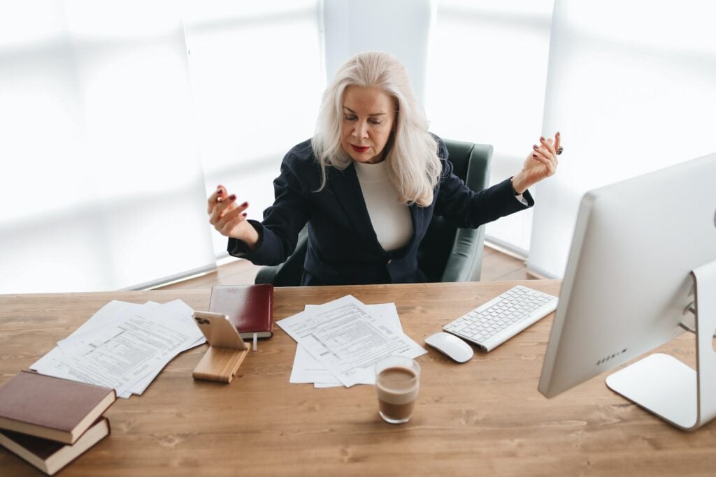 a person sitting at a desk with computer and coffee, stressed about documents lying on desk